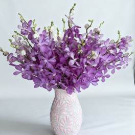 Purple orchid arrangement in a pink-and-white vase