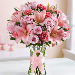 Pink lilies and roses arranged in a clear glass vase with a pink ribbon