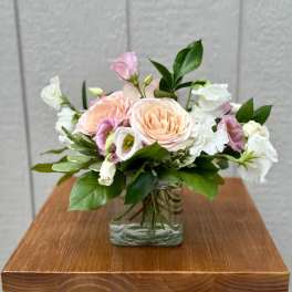 Blush roses and white blooms arranged in a clear glass vase