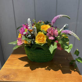 Low basket arrangement with yellow roses, pink blooms, and trailing ivy in a green textured container
