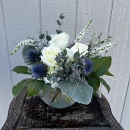 White roses in a glass vase with blue thistle and greenery