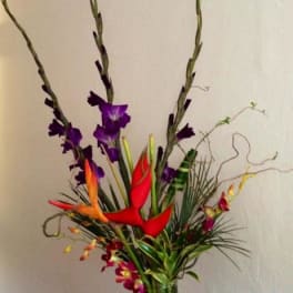 Tall tropical arrangement with red and orange bird-of-paradise and purple orchids in a vase