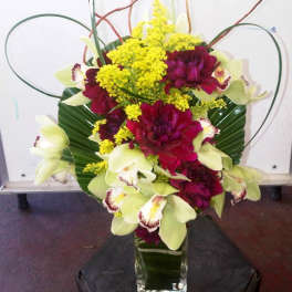 Bouquet of burgundy and pale green orchids with yellow filler in a glass vase