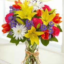 Mixed bouquet of lilies, daisies, and tulips in a glass vase