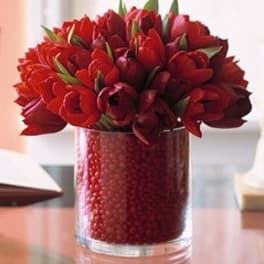 Red tulips arranged in a clear glass vase filled with red beads