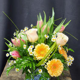 Mixed bouquet with pink tulips, pale roses, and yellow daisies in a patterned vase