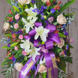 Standing floral spray with white lilies, pale roses, and a purple ribbon bow