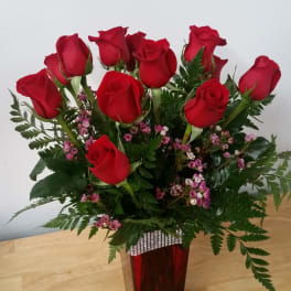 Red roses arranged in a tall vase with pink filler flowers