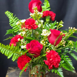 Red roses and carnations in a clear glass vase with fern foliage