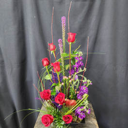 Tall arrangement of red roses and purple flowers in a low black container