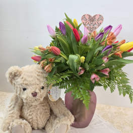Bouquet of multicolored tulips in a pink vase beside a teddy bear