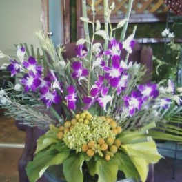 Purple orchids in a low floral arrangement with green leaves and yellow accents