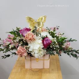Pink and white floral arrangement in a box with a gold butterfly topper