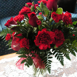 Red roses and carnations in a glass vase with a pink ribbon