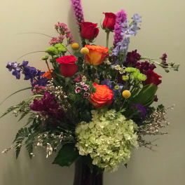 Tall mixed bouquet with roses, hydrangea, and purple accent flowers in a dark vase