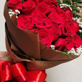 Large bouquet of red roses wrapped in brown paper with white filler flowers and a red ribbon bow.