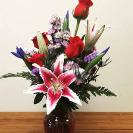 Bouquet of red roses, pink lilies, and purple filler in a dark vase