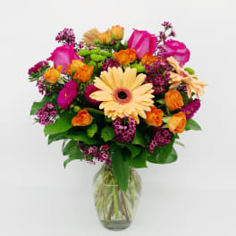 Mixed bouquet of peach gerbera daisies, pink roses, and orange roses in a clear glass vase