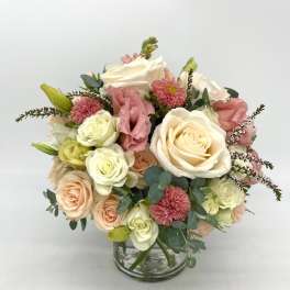 Round arrangement of white and peach roses with pink blooms in a clear glass vase