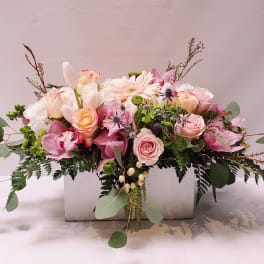 Low pastel arrangement of roses, orchids, and mixed blooms in a white wooden box.