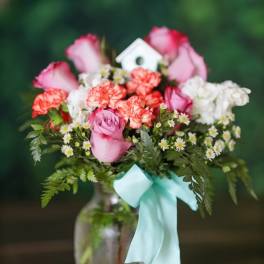 Pink roses and carnations in a glass vase with a blue ribbon