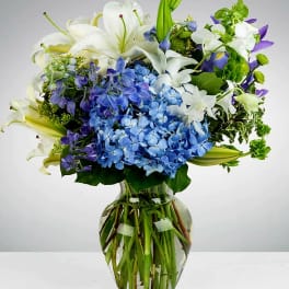 Blue hydrangeas and white lilies in a clear glass vase
