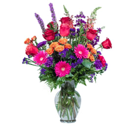 Mixed bouquet of roses, gerbera daisies, and purple flowers in a glass vase