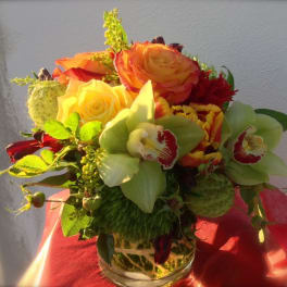 Bouquet of orange and yellow roses with green orchids in a glass vase