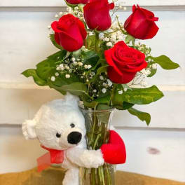 Red roses in a glass vase with a white teddy bear