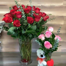 Two rose bouquets in glass vases, one with a teddy bear and heart