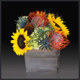 Bright mixed bouquet with sunflowers and exotic blooms in a wooden container