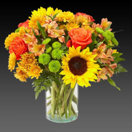 Bouquet of sunflowers, orange roses, and yellow mums in a glass vase