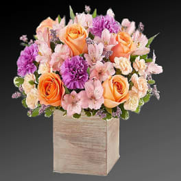 Bouquet of peach roses, purple carnations, and pink flowers in a wooden cube vase