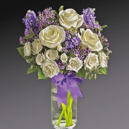 White roses and purple flowers in a glass vase with a purple ribbon