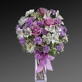 Purple and white bouquet in a clear glass vase with a ribbon