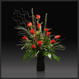 Red roses arranged in a tall black vase with curly decorative stems