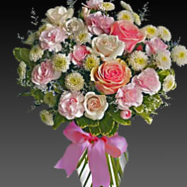Pink and white rose bouquet in a striped glass vase with a pink ribbon