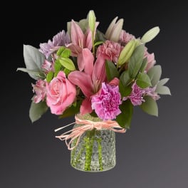 Pink and purple bouquet in a glass vase with a ribbon tie