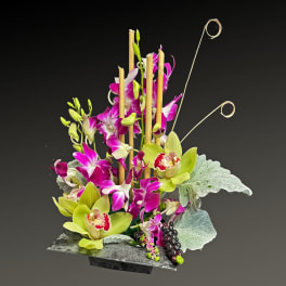 Tall orchid arrangement in a dark rectangular vase with decorative bamboo loops
