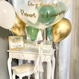 Cluster of gold, white, and green balloons with a large clear balloon reading congratulations