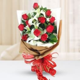 Bouquet of red roses with white lilies wrapped in brown paper and tied with a red ribbon