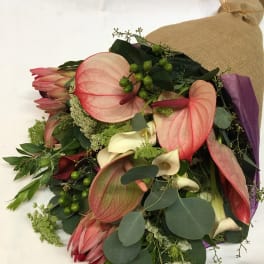 Bouquet with pink anthuriums, cream calla lilies, and dark greenery wrapped in burlap