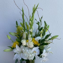 Tall white floral arrangement in a clear glass vase with lilies, roses, and orchids