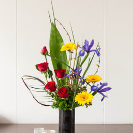 Tall bouquet of red roses, yellow daisies, and purple irises in a black vase