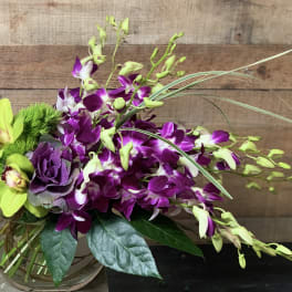 Purple orchids and green flowers in a glass vase