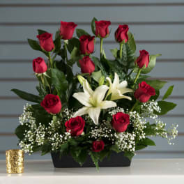 Low arrangement of red roses and white lilies in a black container with baby's breath accents.