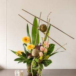 Tall floral arrangement with yellow blooms, pink tulips, and decorative branches