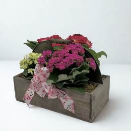 Pink and red flowers arranged in a wooden box with a floral ribbon
