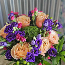 Peach roses and purple lisianthus in a round bouquet