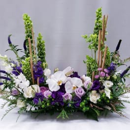 Purple and white floral arrangement with orchids and roses in a low design